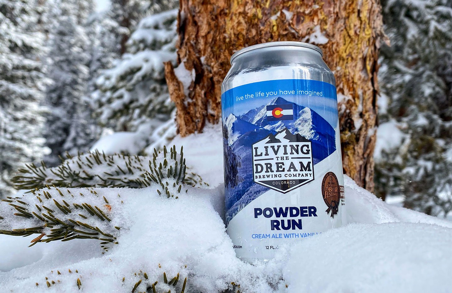 Can of Powder Run Cream Ale beer sitting in a snow pile at the base of a pine tree
